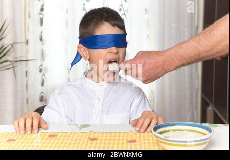 Prova del gusto, bendato caucasico ragazzo provando un cucchiaio di riso. Foto Stock