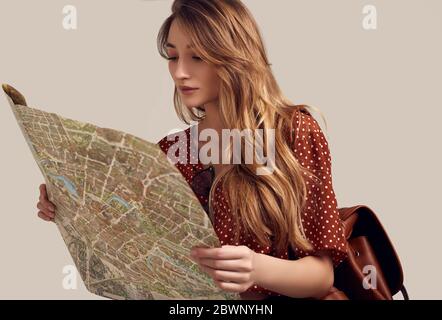 Concetto di viaggio. Sognare il viaggio. Studio ritratto di bella giovane donna hipster con zaino tenendo mappa. Isolato su sfondo grigio Foto Stock