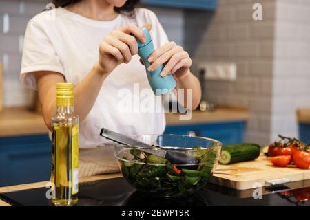 Immagine tagliata di una giovane donna che cucinava insalata mentre si è in piedi al banco della cucina, peppering Foto Stock