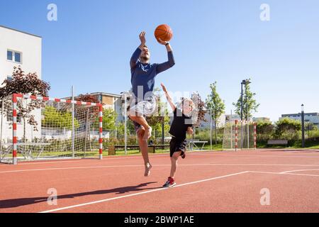 Papà e figlio giocano a piedi nudi di basket con la palla su un parco giochi Foto Stock