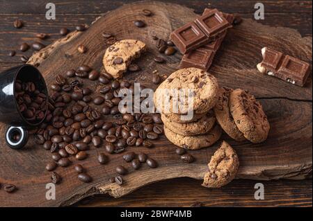 Biscotti, pezzi di cioccolato e caffè in grani su un asse di legno Foto Stock