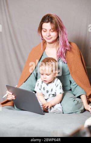 Rimani a casa, mamma lavora in remoto su un computer portatile, prendendosi cura del bambino. Una giovane madre in congedo di maternità sta cercando di lavorare come freelance w Foto Stock