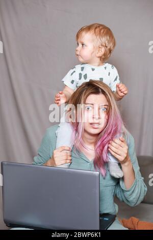 Rimani a casa, mamma lavora in remoto su un notebook, prendendosi cura del bambino. Una giovane madre in congedo di maternità sta cercando di lavorare come freelance con un bab Foto Stock