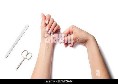 Le mani femminili tengono le forbici per unghie, accanto ai dispositivi di posa per la cura delle unghie. La ragazza fa un manicure. Isolato su sfondo bianco. Vista dall'alto. Foto di alta qualità Foto Stock