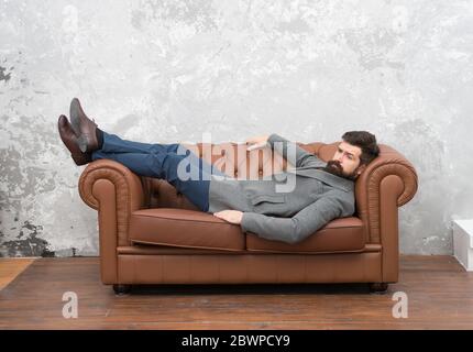 Aspetto bello e soggiorno di moda. Brutale hipster rilassarsi sul divano. Uomo bearded con look di moda. Moda e stile uomo. Abbigliamento casual per affari. Negozio di abbigliamento da uomo. Moda unica come voi. Foto Stock