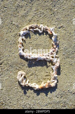 Il numero nove (9) è disposto su una spiaggia al sole fatta di piccoli pezzi di corallo bianco e arancio Foto Stock