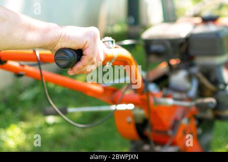 L'uomo coltivatore aratura la terra con un coltivatore. Macchine agricole: Coltivatore per dissodamento in giardino,motocoltivatore.. Foto Stock