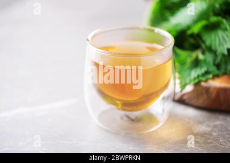 Tazza di sano tè alle erbe con ortica. Medicina alternativa di erbe. Nettle di pungitura, urtica. Cura delle allergie cutanee. Nettle fresche su dorso grigio Foto Stock