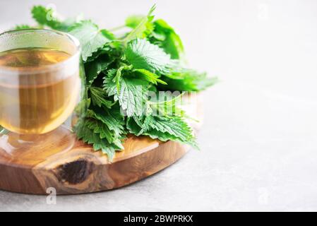 Tazza di sano tè alle erbe con ortica. Medicina alternativa di erbe. Nettle di pungitura, urtica. Cura delle allergie cutanee. Nettle fresche su dorso grigio Foto Stock