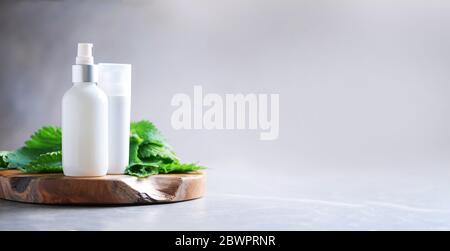 Crema di ortica, crema, shampoo o sapone in bottiglia bianca e foglie di bollitori fresche su sfondo grigio. Erbe medicinali per la salute e la bellezza, la cura della pelle e. Foto Stock