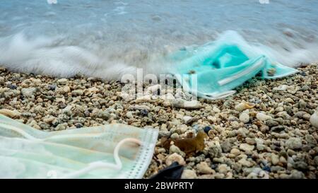 Rifiuti di plastica del coronavirus che inquinano l'ambiente. Maschere monouso scoppio rifiuti in oceano. Gettato usato usa e getta maschera medica galleggia in se Foto Stock