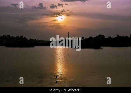 Un'alba bellissima vicino ad un lago dove un uccello sta nuotando nel lago. Il riflesso del sole può essere visto e la sagoma dell'uccello può essere vista Foto Stock