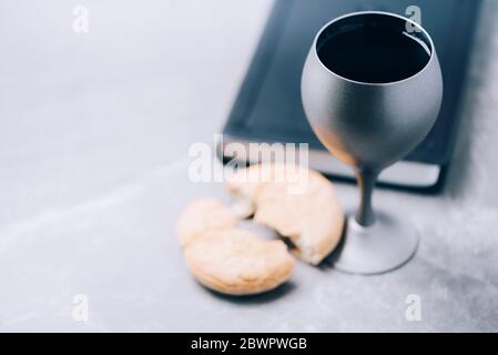 Pane azzimo, calice di vino, Sacra Bibbia su sfondo grigio. Comunione cristiana per ricordare il sacrificio di Gesù. Pasqua. Eucaristia Foto Stock