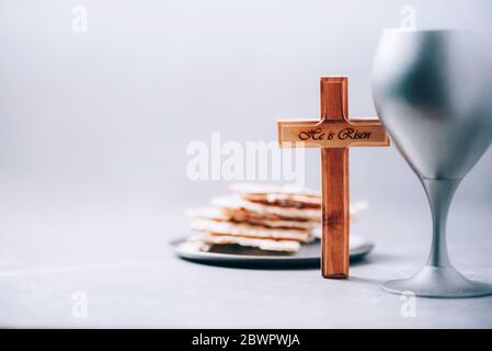 Pane azzimo Matzos, calice di vino, croce di legno su fondo grigio. Comunione cristiana per ricordare il sacrificio di Gesù. Pasqua Foto Stock