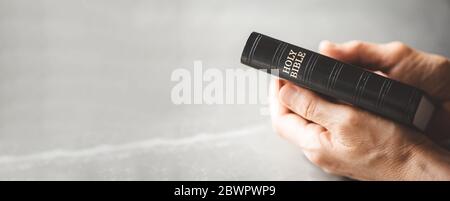 Mani che tengono la Bibbia Santa su sfondo grigio. Condividere il Vangelo con i giovani. Spazio di copia. Concetto cristiano Foto Stock