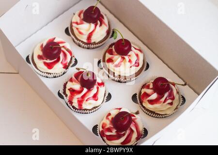 Cupcake alla vaniglia in scatola regalo con salsa di frutti di bosco, panna montata e ciliegie fresche sulla parte superiore. Messa a fuoco selettiva. Foto Stock