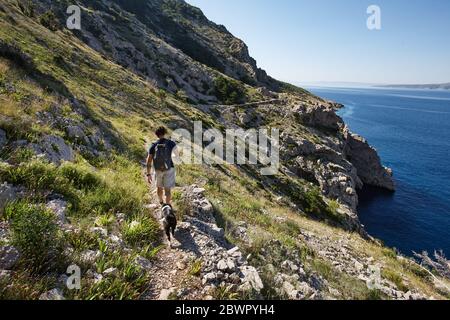 Uomo arrampicata clifs con il suo cane lungo il mare in estate mattina, Croazia Foto Stock