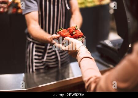 Primo piano venditore in grembiule a strisce dietro il bancone dando fragole al cliente in un moderno supermercato isolato Foto Stock