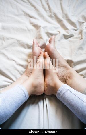 Madre e bambino si uniscono i piedi insieme mentre si siedono su alcune lenzuola beige. È un momento tenero come confrontano quanto simili sono. Primo piano.