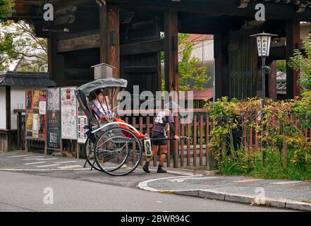 KYOTO, GIAPPONE - 18 OTTOBRE 2019: Un risciò tirato (o risciò) guida un carretto passeggero a due ruote con il turista vestito da maiko sulla strada Foto Stock