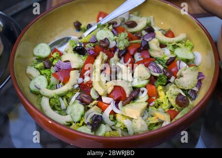 Insalata fresca con avocado, olive, pomodori e altri ingredienti sani in una ciotola rustica, focalizzazione selezionata, profondità di campo stretta Foto Stock