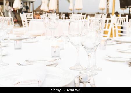 Servizio festivo con bicchieri per una celebrazione all'aperto con lampade da garland e palme sullo sfondo. Matrimonio, anniversario, cena di compleanno e festa. Immagine a toni con posizione per il testo Foto Stock