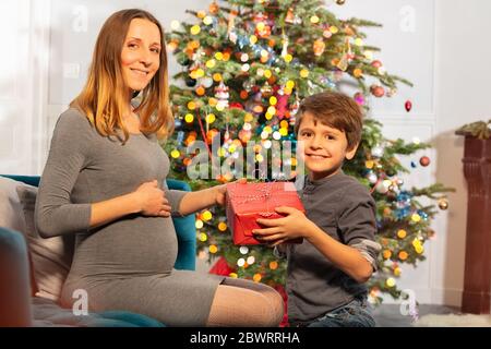 Madre incinta e bambino che riceve regalo di Natale vicino albero di Capodanno Foto Stock