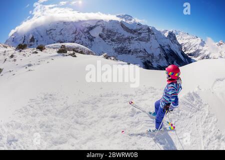 Ritratto dall'alto di una ragazza sulla pista da sci in cima a una montagna e guarda giù sulla valle con casco rosa Foto Stock