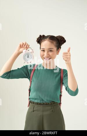 Giovane donna che tiene la sveglia classica su sfondo chiaro felice con il sorriso grande che fa il segno di ok, pollice in su con le dita, segno eccellente Foto Stock