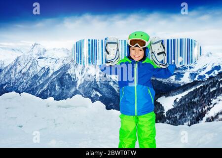 Ritratto anteriore di un ragazzo tiene lo snowboard sulle spalle sopra l'alta montagna Foto Stock