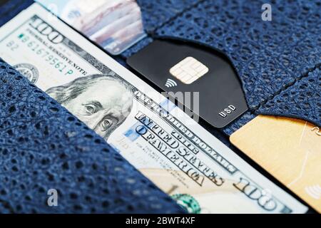 In pelle partman in blu con un centinaio di dollari fatture e carte di credito elettronico su uno sfondo nero. Foto Stock