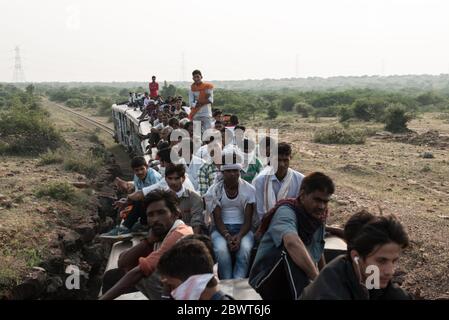 Uomini in cima a un treno sovraffollato che passa attraverso la campagna a Madhya Pradesh, India. Ferrovie indiane. Foto Stock