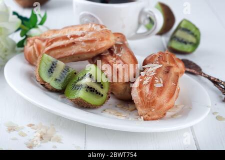 eclair con tazza di caffè e kiwi su sfondo bianco di legno. Foto Stock