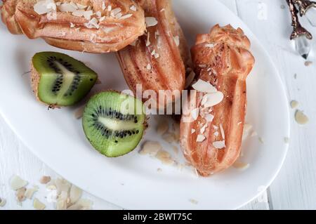 eclair con tazza di caffè e kiwi su sfondo bianco di legno. Foto Stock