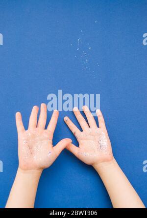 Mani per bambini con glitter e confetti di colore blu e argento su sfondo blu classico. Foto Stock