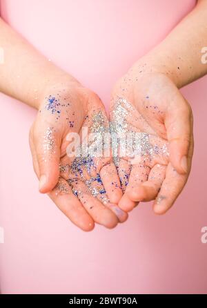 Mani del bambino con glitter color argento su sfondo rosa pastello. Foto Stock