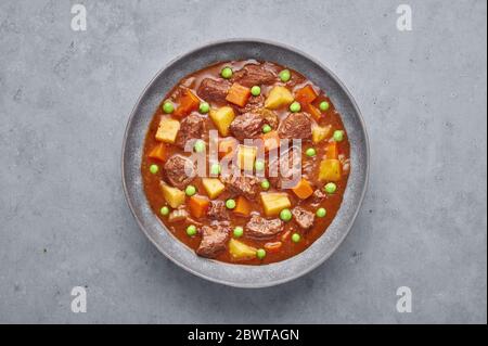 Stufato di manzo irlandese in ciotola grigio opaco su fondo di cemento. Stufate con carne di manzo o di agnello con patate, carote, piselli ed erbe. tradizionale americano e. Foto Stock