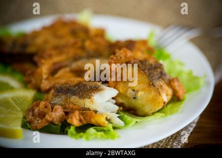 pesce di nasello fritto in pastella con lattuga e limone in un piatto Foto Stock