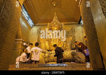 I devoti maschili attaccano foglie dorate alla statua del Buddha Mahamuni. Mandalay, Myanmar Foto Stock