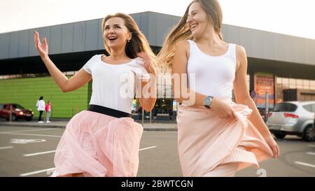 Ritratto di due ragazze ridenti allegre nello stesso vestito che gioca e che si divertono nel parcheggio auto al centro commerciale Foto Stock