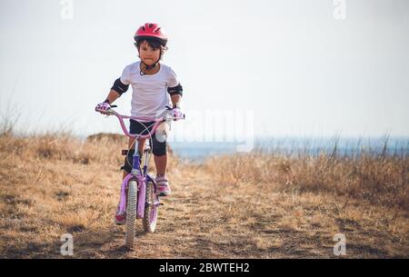 Bambina con percorsi in bicicletta al tramonto sulle colline Foto Stock