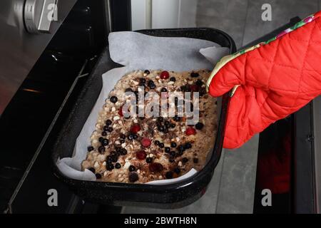 Mano della ragazza con i guanti protettivi della cucina mettere la pizza vegetariana di frutta dolce con le bacche nel forno. Pizza fresca in casseruola in cucina casalinga Foto Stock