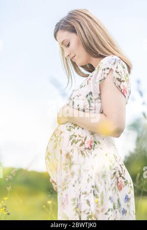 Bella donna incinta in bianco abiti estivi in prato pieno di giallo flovers fioritura. Foto Stock