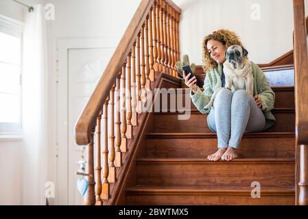 Donna seduta sulle scale, utilizzando uno smartphone con un pug in grembo Foto Stock