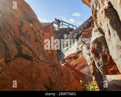 Donna in una ringhiera di legno tra le rocce, Robberg Riserva Naturale, Sud Africa Foto Stock