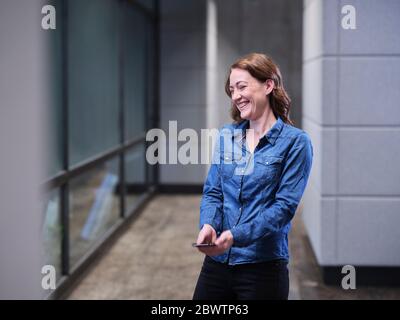 Donna d'affari ridente usando il telefono delle cellule sul pavimento moderno dell'ufficio Foto Stock