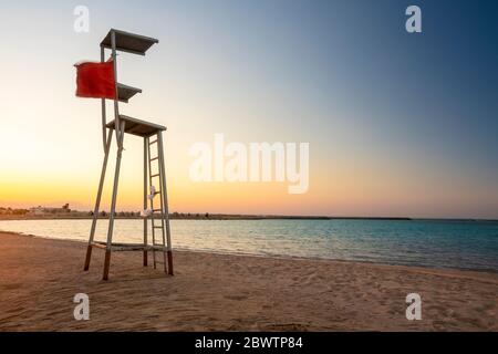 Egitto, Hurghada, sedia salvagente vuota in piedi sulla spiaggia costiera sabbiosa della baia di Sahl Hasheesh al tramonto Foto Stock