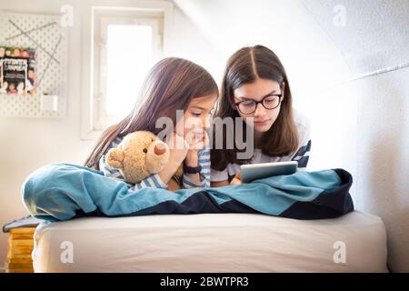 Sorelle che usano la tavoletta sdraiata sul letto Foto Stock