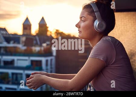 Giovane donna che ascolta musica con le cuffie sul balcone al tramonto