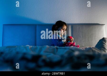 Bambina seduta a letto che gioca con il suo giocattolo Foto Stock